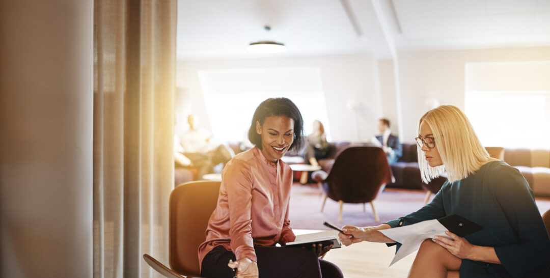 Smiling businesswomen discussing work on a laptop in an office Smiling businesswomen discussing work on a laptop in an office