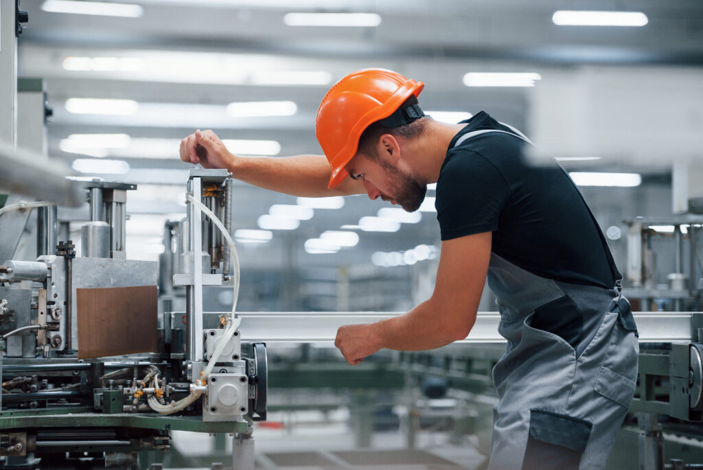 Operator of machine. Industrial worker indoors in factory. Young technician with orange hard hat