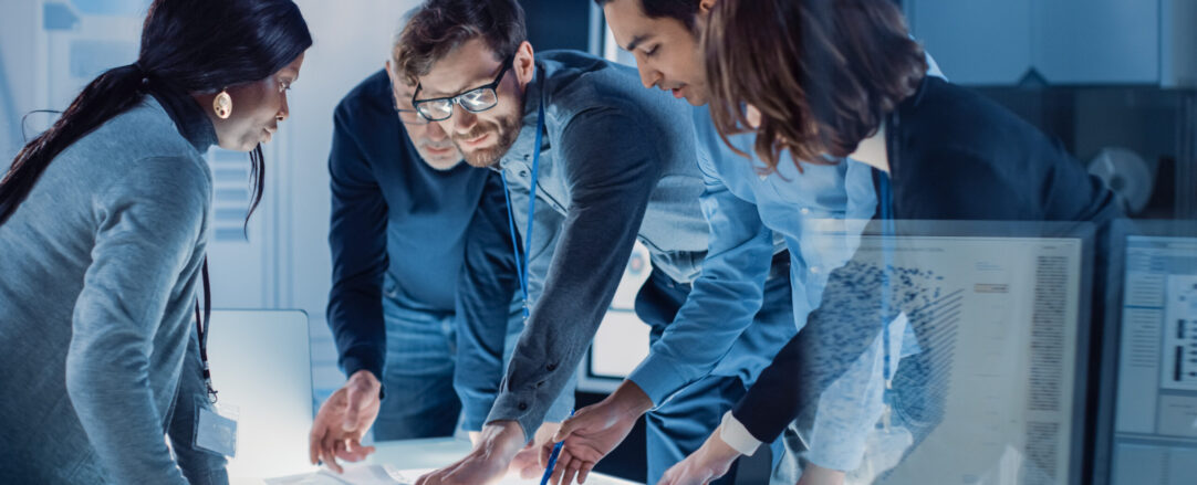 Engineers Meeting in Technology Research Laboratory: Engineers, Scientists and Developers Gathered Around Illuminated Conference Table, Talking and Finding Solution, Inspecting and Analysing Industrial Engine Design.