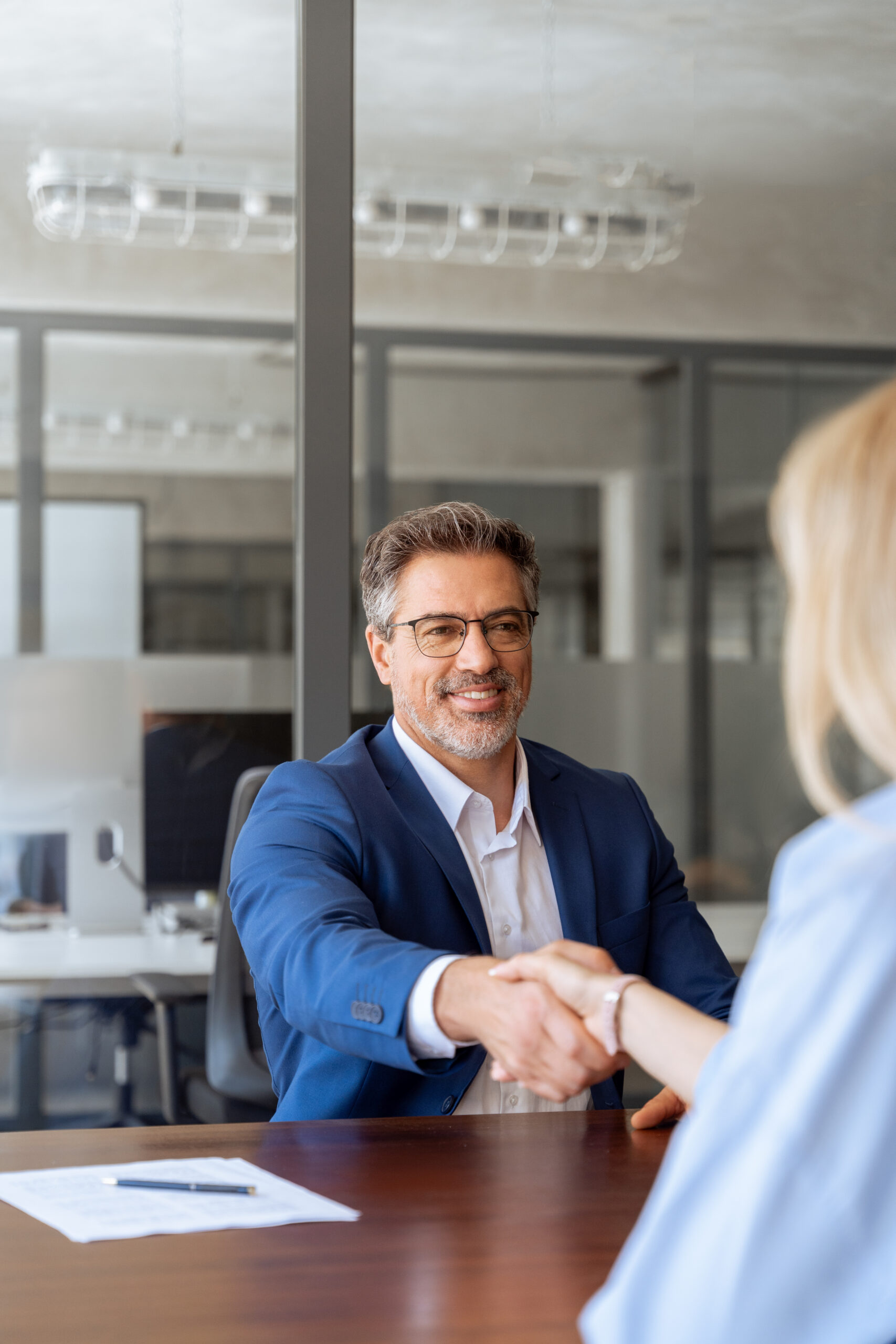 Mature Latino bank worker man shaking hand with client, recruit female employee or business partner after signing a contract. Group of people satisfied with results of team work together. Vertical