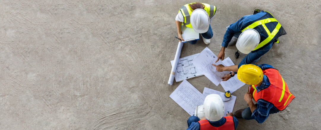 Top view of engineer, architect, contractor and foreman meeting at a construction building site with floor plan for real estate development